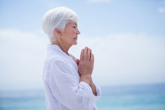 Side view of senior woman with hands clasped at beach against sky