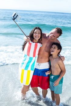 Cheerful family taking selfie while standing in shallow water at sea shore