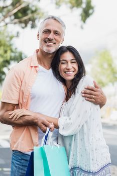 Portrait of happy couple with shopping bags embracing outdoors
