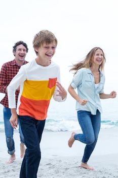 Cheerful family running at sea shore against sky
