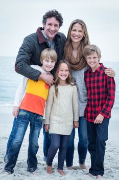 Full length portrait of cheerful family standing at sea shore against sky