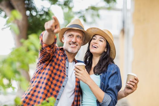 Man pointing to woman with coffee while standing outdoors
