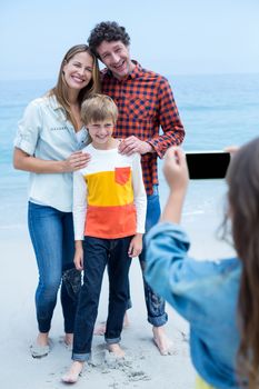 Girl photographing happy family with mobile phone at sea shore