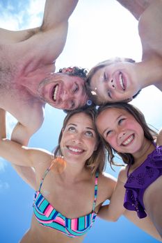 Directly below shot of cheerful family huddling against bright sky