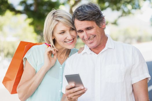 Couple using cellphone while smiling outdoors