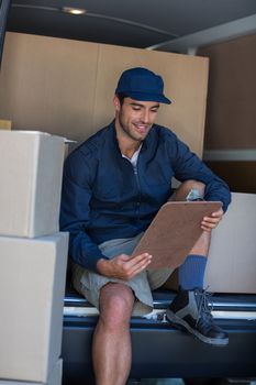 Smiling delivery person with clipboard while sitting in van