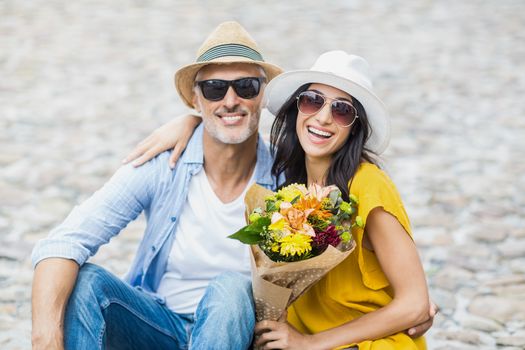 Portrait of happy couple with bouquet sitting outdoors