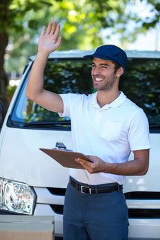 Smiling delivery man waving hand while standing by van