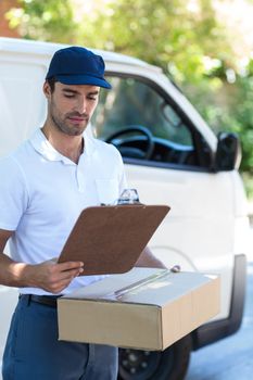 Delivery man looking at clipboard while standing by van
