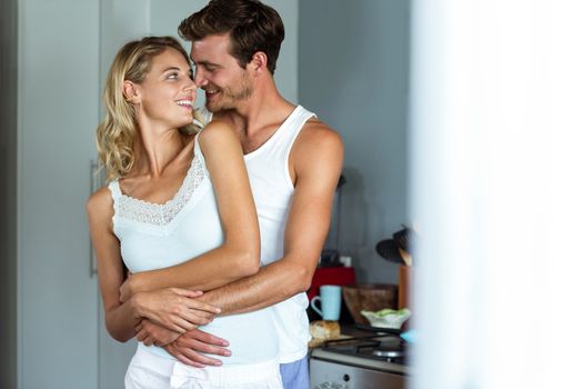 Romantic young couple embracing while looking at each other in kitchen at home