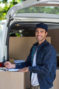 Portrait of delivery person writing in clipboard while standing by van