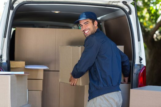 Portrait of happy delivery man loading cardboard box in van