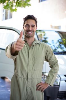 Portrait of smiling pesticide worker showing thumbs up while standing by van