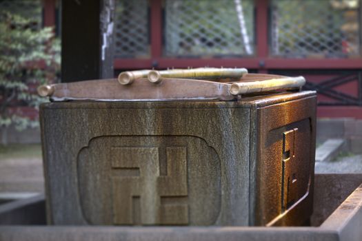 Temizuya "手水舎" stone adorned with the Buddhist swastika cross used for ablution of purification in the enclosure of Nezu shrine of the 18th century in Tokyo.