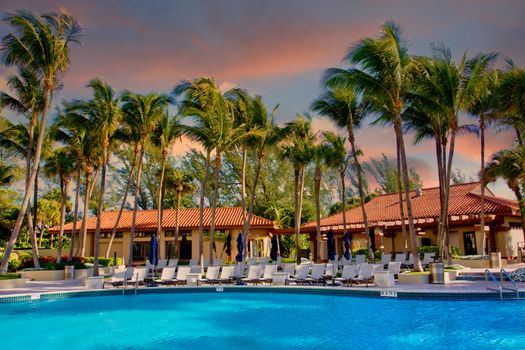 Stucco and tile roof cabanas and palm trees next to a resort swimming pool