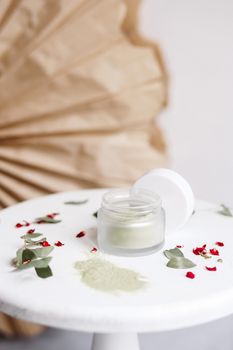 Powder cosmetic mask. Glass jar with matcha on a white background with dry petals