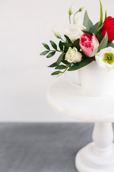 Spring bouquet in white vase on wooden white stand. Roses, tulips and lisianthus