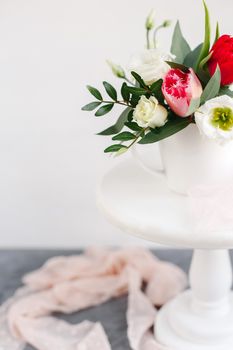 Spring bouquet in white vase on wooden white stand. Roses, tulips and lisianthus