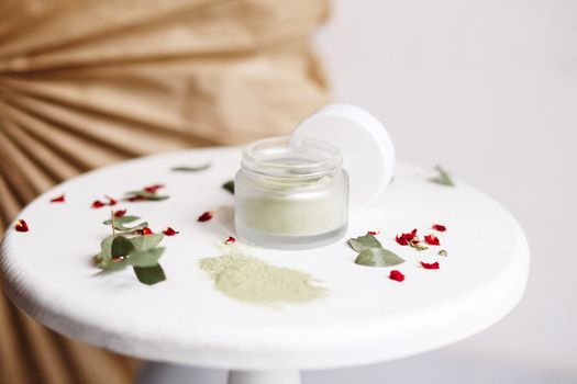 Powder cosmetic mask. Glass jar with matcha on a white background with dry petals
