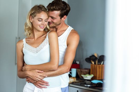 Romantic young man embracing woman from behind in kitchen at home