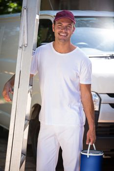 Portrait of painter holding stepladder and bucket standing near his van