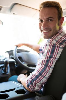 Portrait of young man looking at camera while sitting on cars front seat