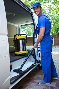 Portrait of happy janitor cleaning the car with vacuum cleaner