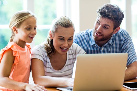 Father looking at mother and daughter using laptop in house 