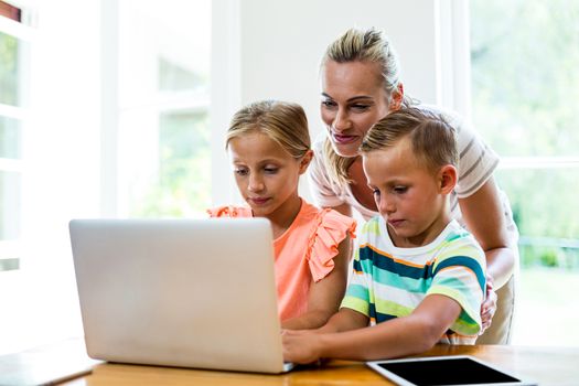 Mother teaching children while using laptop at home 