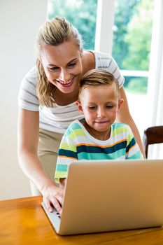 Smiling mother teaching son while using laptop at home 
