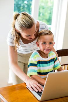 Happy mother and son using laptop at table in home 