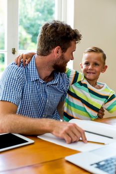 Smiling father with tablet teaching son at home 