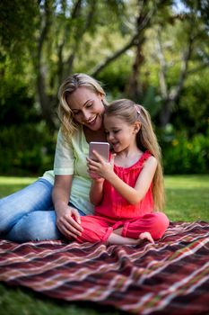 Smiling daughter showing phone to mother while sitting in yard 