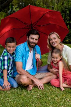 Portrait of smiling family sitting with umbrella in yard 