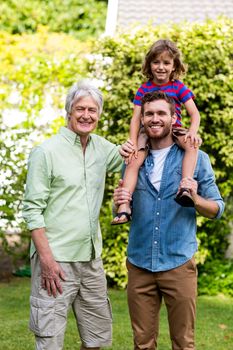 Portrait of grandfather standing with son carrying grandson at yard 