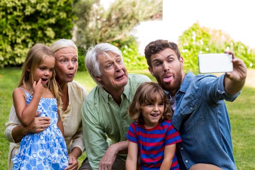 Happy family making face while taking selfie with family while sitting in yard