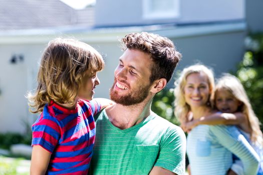 Happy parent carrying children in yard against house