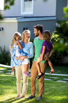 Smiling parents carrying children in yard against house