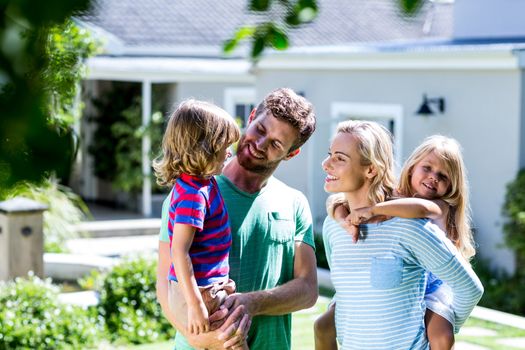 Cheerful parent carrying children in yard against house