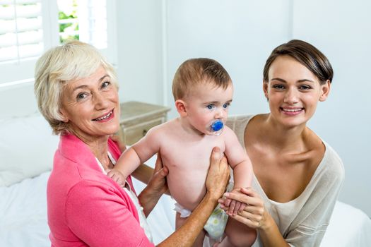 Happy grandmother and mother with baby boy on bed at home