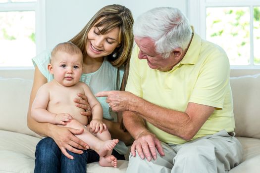 Happy grandfather and mother with baby boy on sofa at home