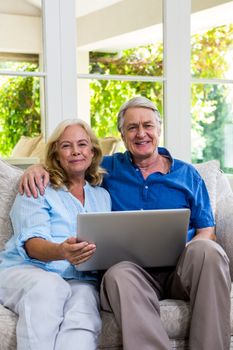 Portrait of senior couple holding laptop while sitting in living room at home