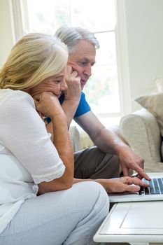 serious senior couple using laptop while sitting in living room at home