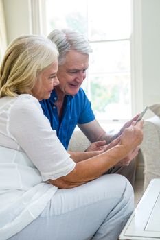Happy senior couple using digital tablet while sitting in living room at home