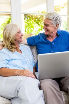 Happy senior couple with laptop while sitting on sofa in living room at home