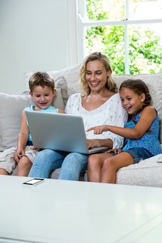 Happy children with mother using laptop while sitting on sofa