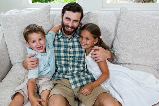 Portrait of cheerful father with son and daughter on sofa