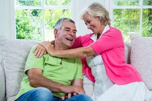 Romantic senior woman laughing with husband on sofa at home