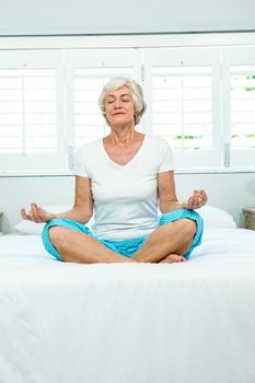 Aged woman doing yoga against window on bed at home