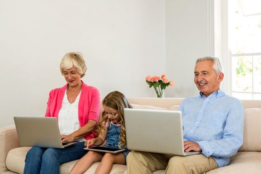 Happy grandparents and girl using technology while sitting on sofa